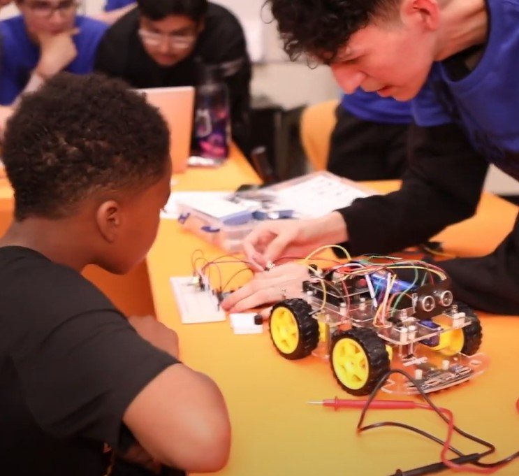 Older student helping a younger student build a robot